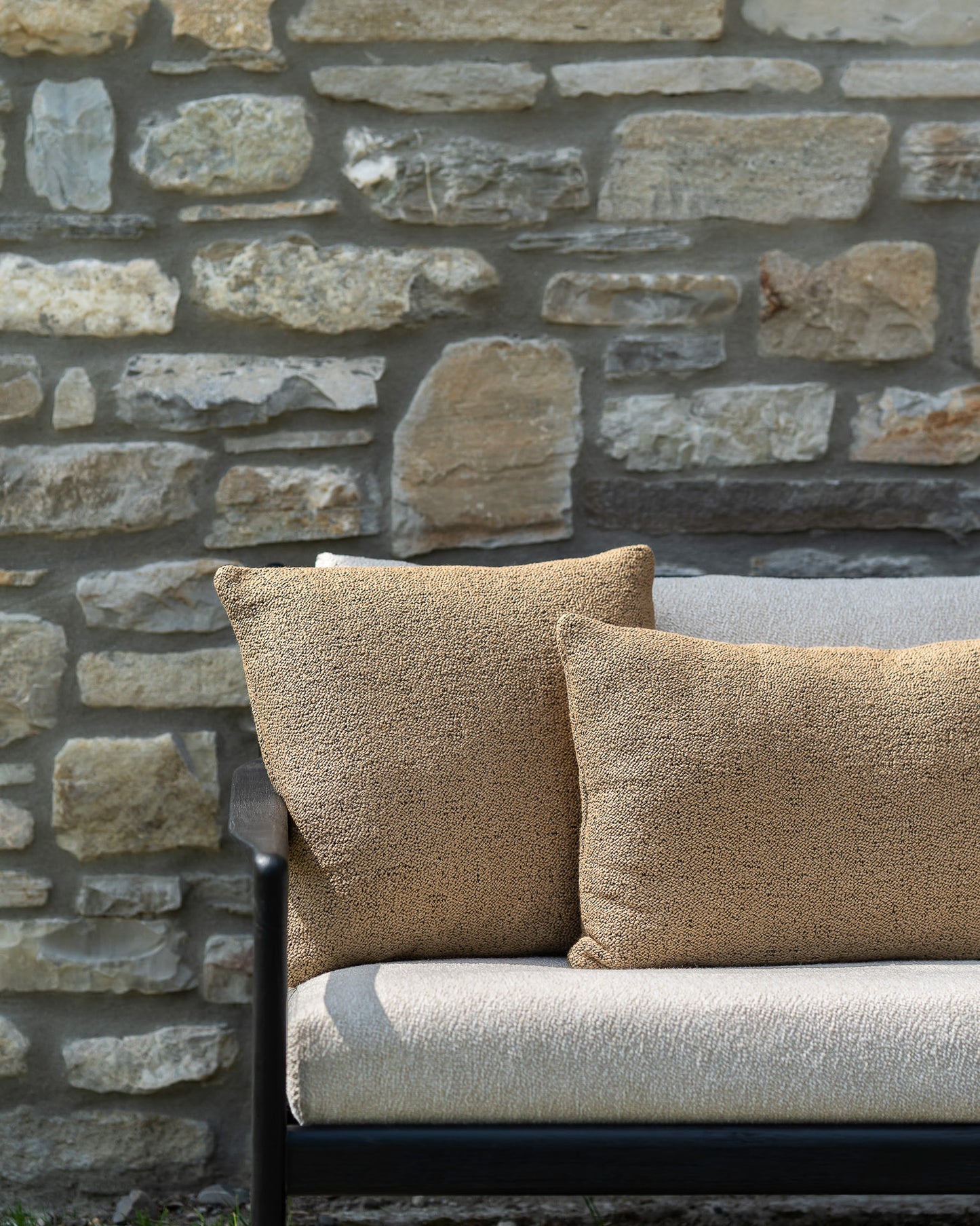 Ethnicraft Nomad Outdoor Cushion Cumin on jack outdoor black bench with natural upholstery against stone wall, two sizes cushions