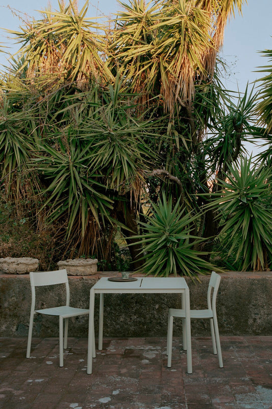 New Work May Chair Light Grey without armrest with complimentary table next to tropical plants outdoor.