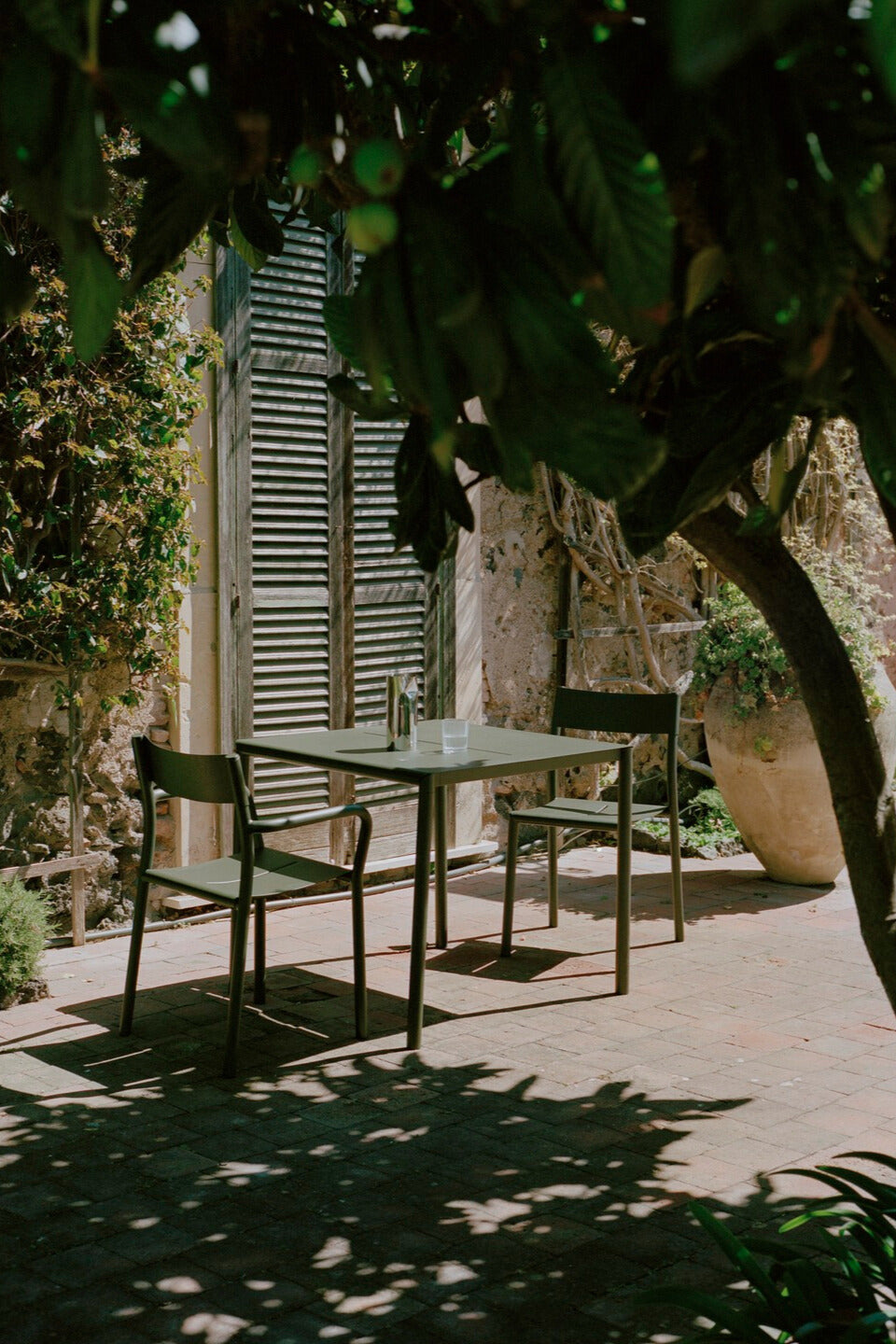 new works may chair dark green with table outdoor with pleat pitcher on it trees and shadow