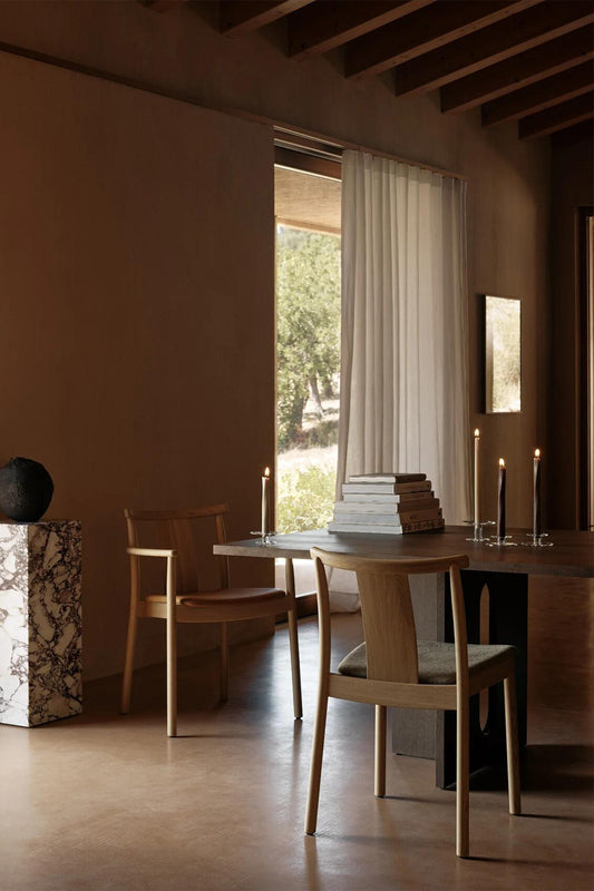 The Merkur Dining Chair from Audo Copenhagen with books and candles on the dining table.