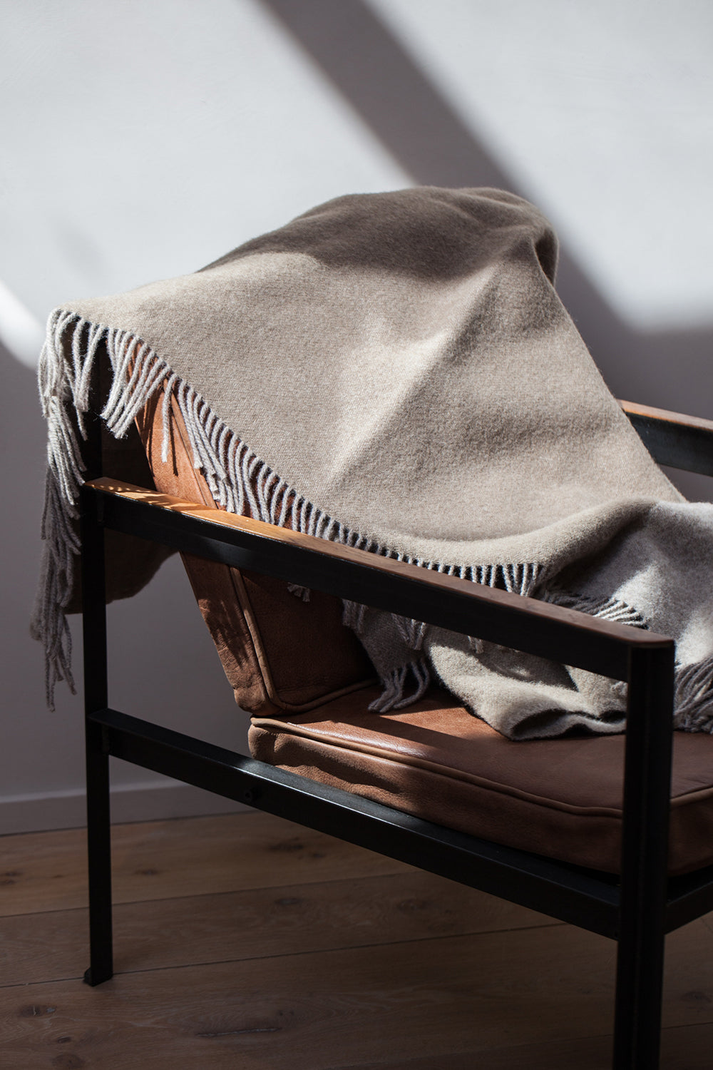 Earth Fawn Blanket by Forestry Wool displayed on a leather chair, adding a cozy and inviting touch to the space.