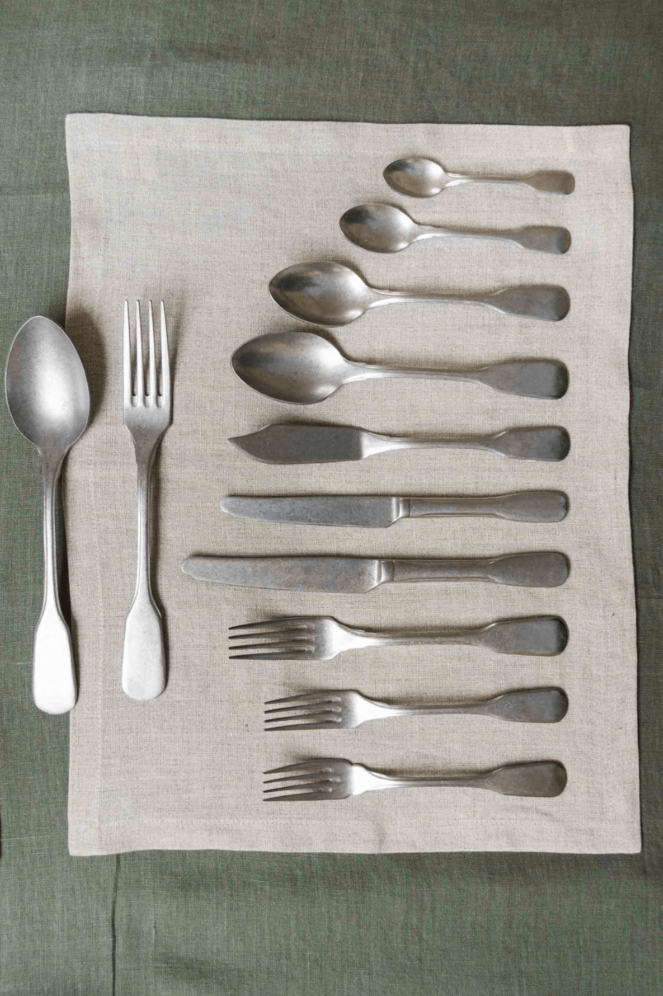 Silver cutlery collection set on white linen napkin and green linen table cloth.