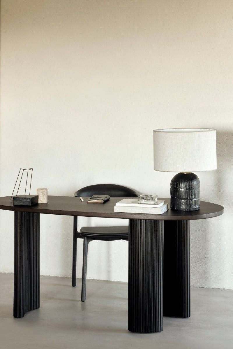 The Boomerang Desk by Ethnicraft with desk items on it and a table lamp on the right.