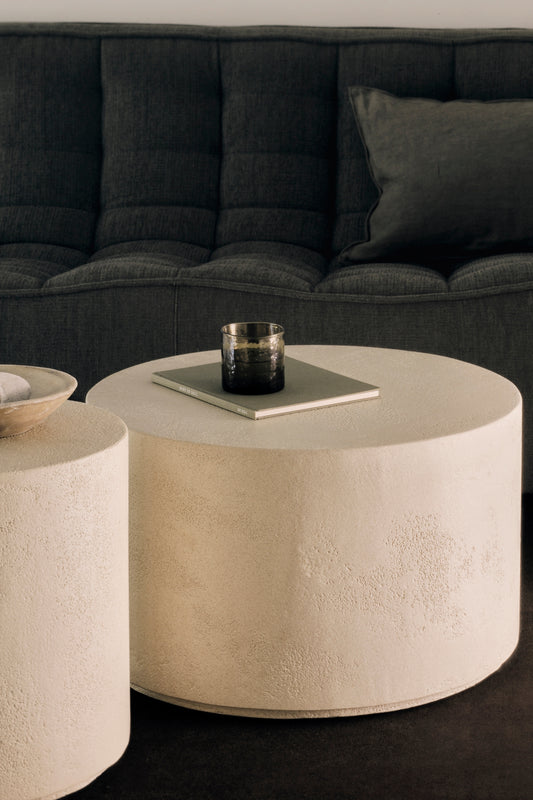 A close up of the Elements Coffee Table Round by Ethnicraft. With a class and a book on top of the table.