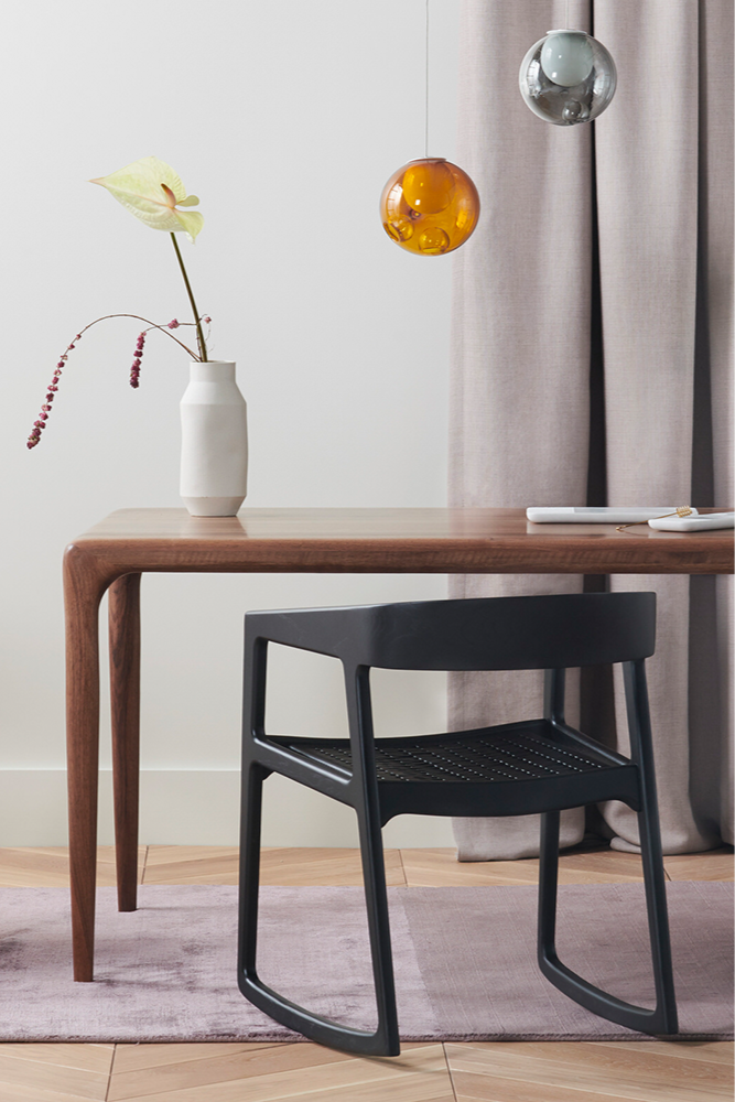 The Lakri Dining Table in Walnut by Artisan with a black dining chair