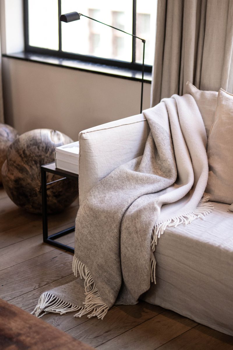 Duo Wool Blanket displayed on a sofa, adding a cozy and inviting touch to the space. Its generous size and lightweight design make it versatile for various settings.