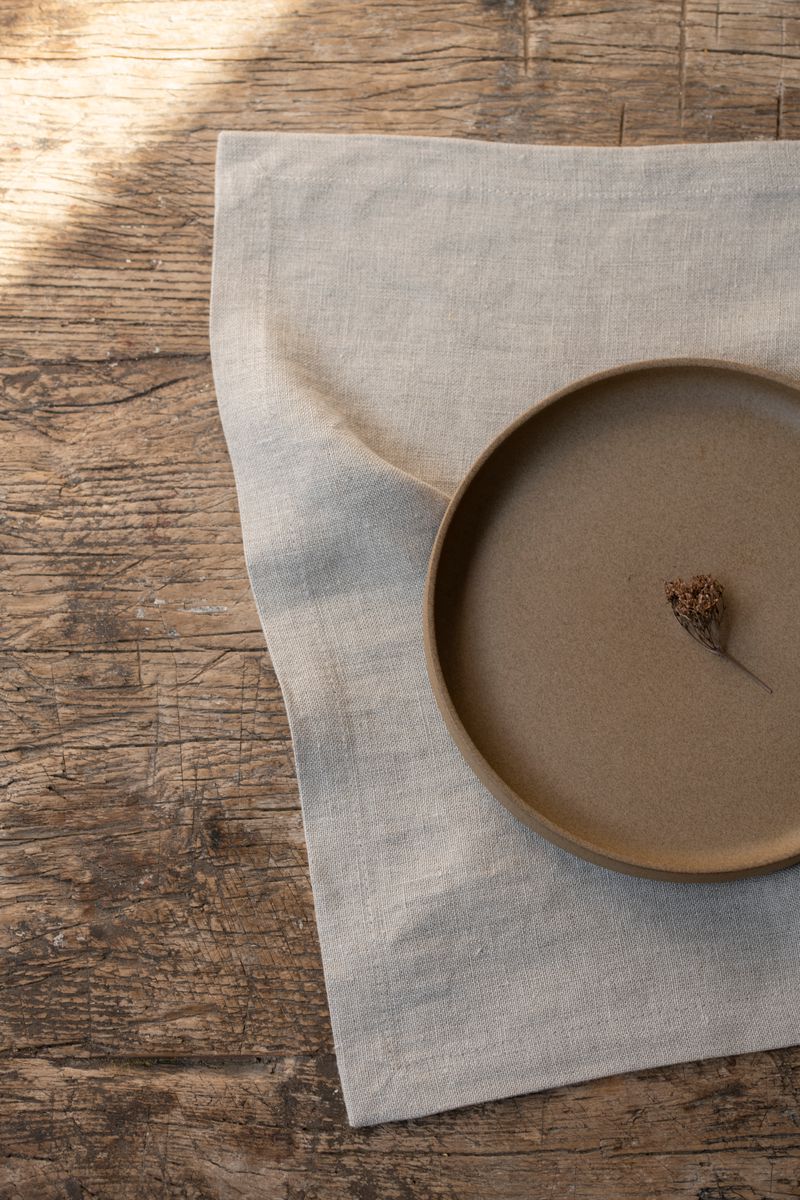 Linen Placemat by Timeless Linen set on wooden table with plate and flower.