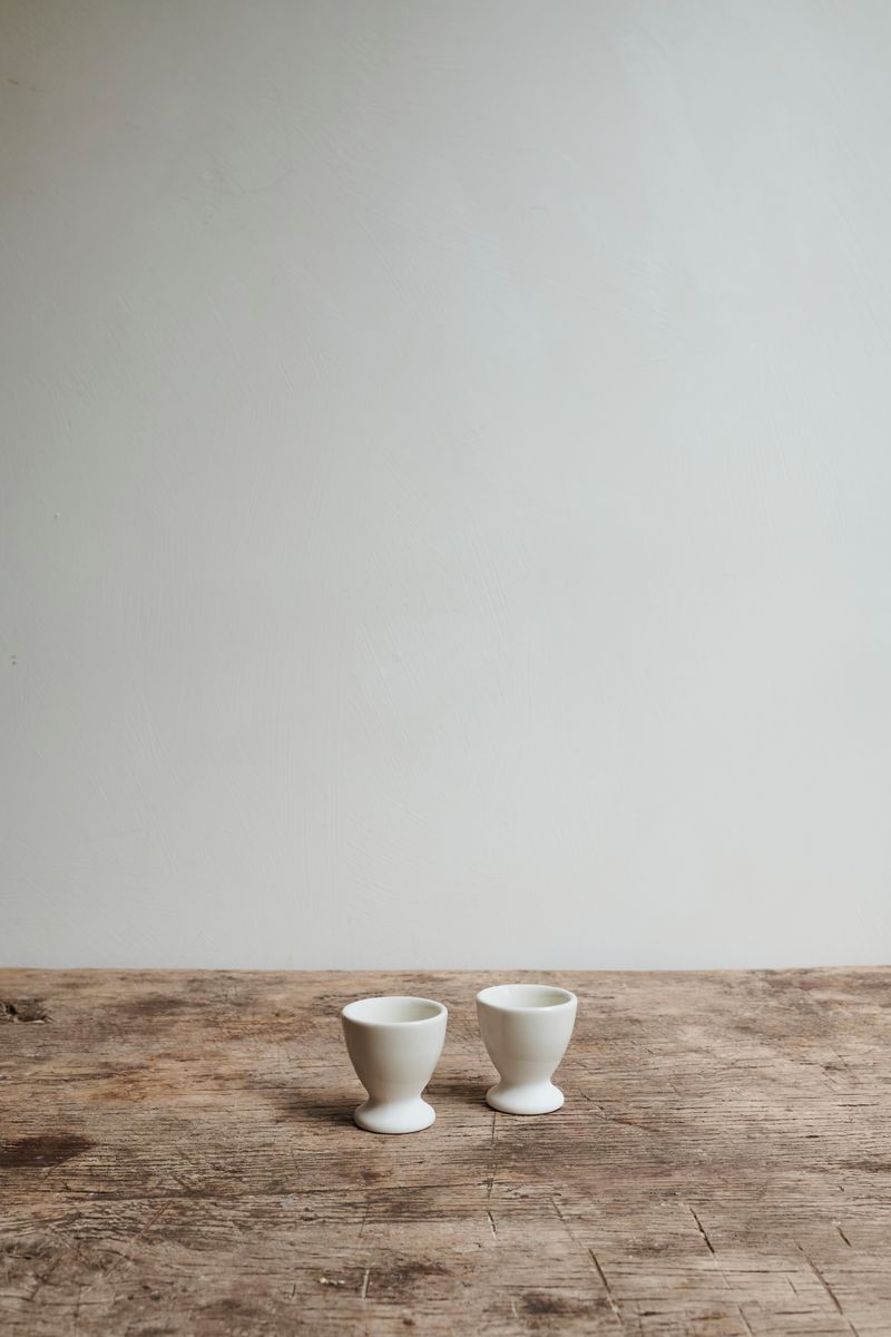 Two ceramic white egg cups on wooden table.
