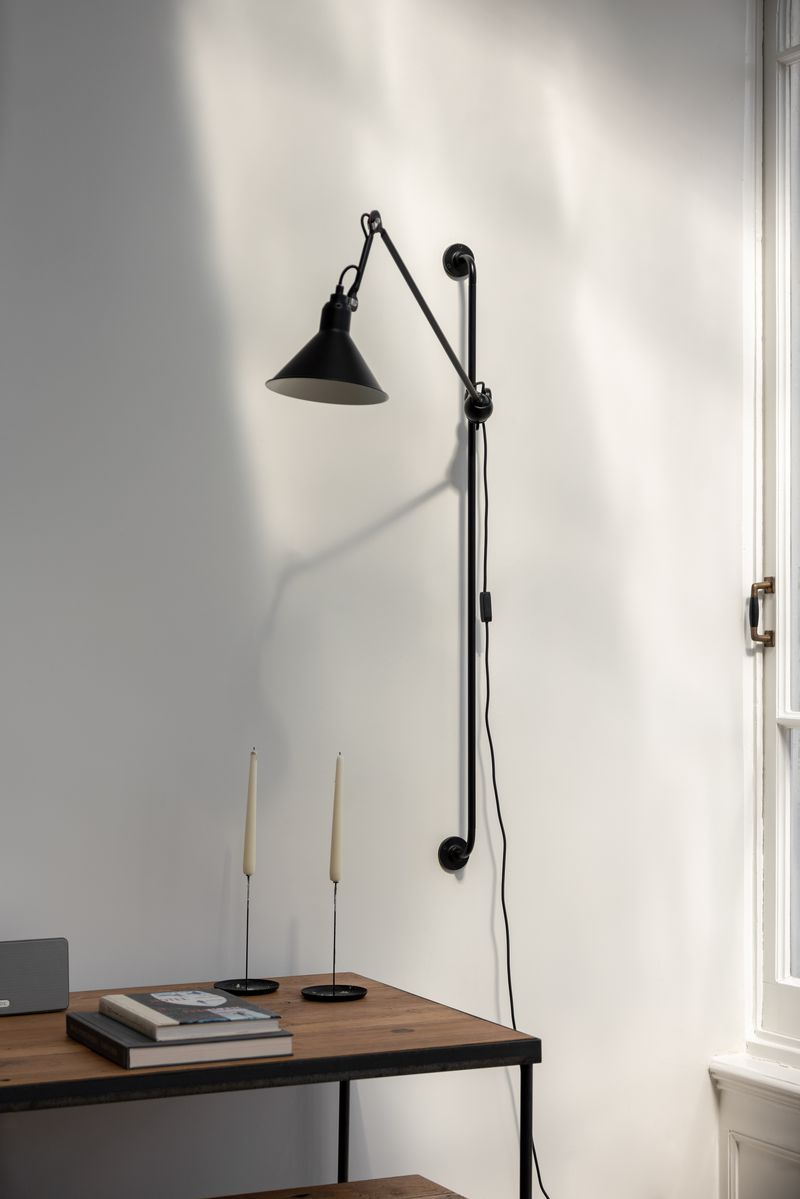 DCW Editions Lampe Gras N°214 wall lamp illuminating a cozy corner. Stylish and versatile with a vintage-inspired touch.