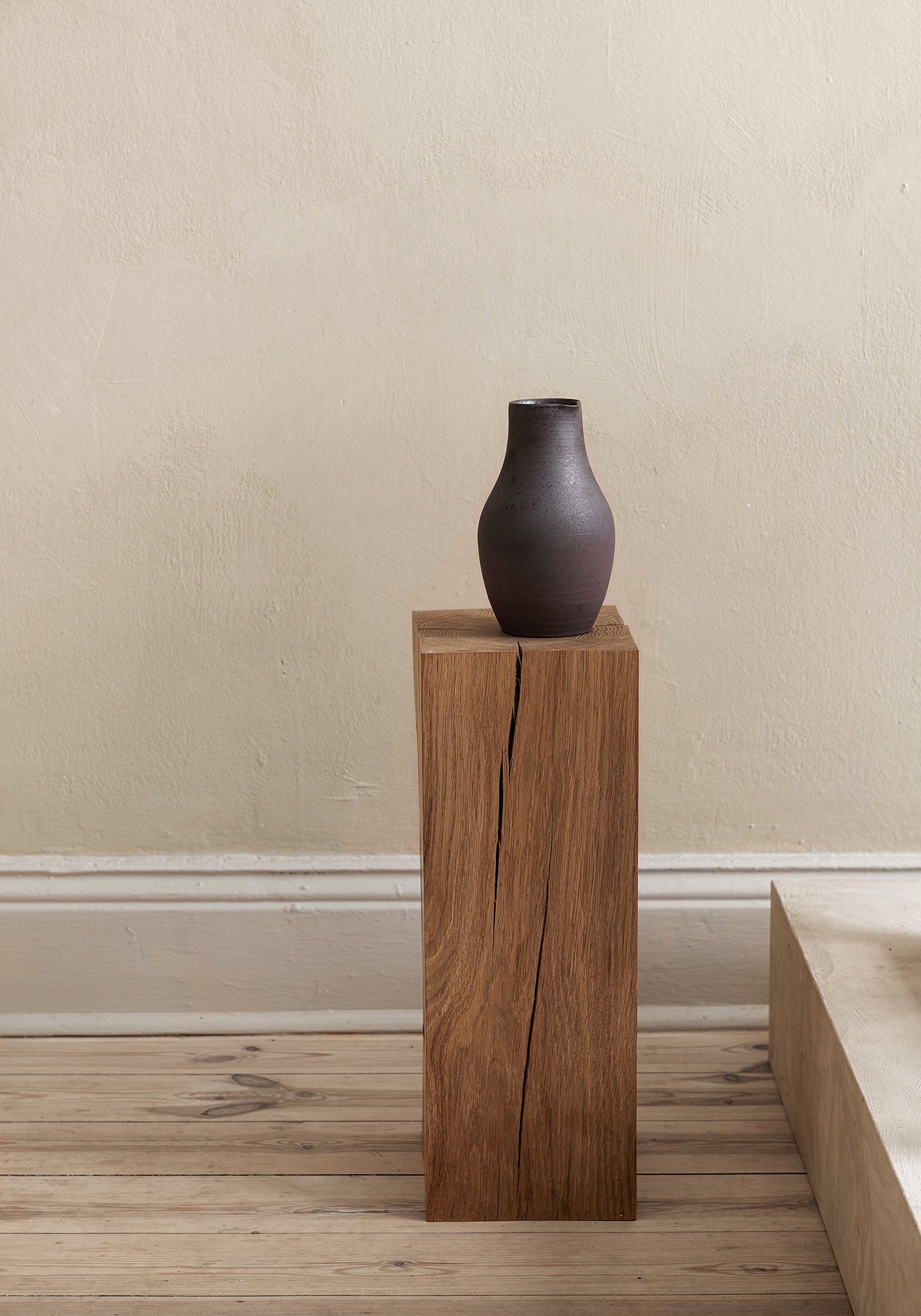Black ceramic sake jug set on a display pedestal in neutral interior