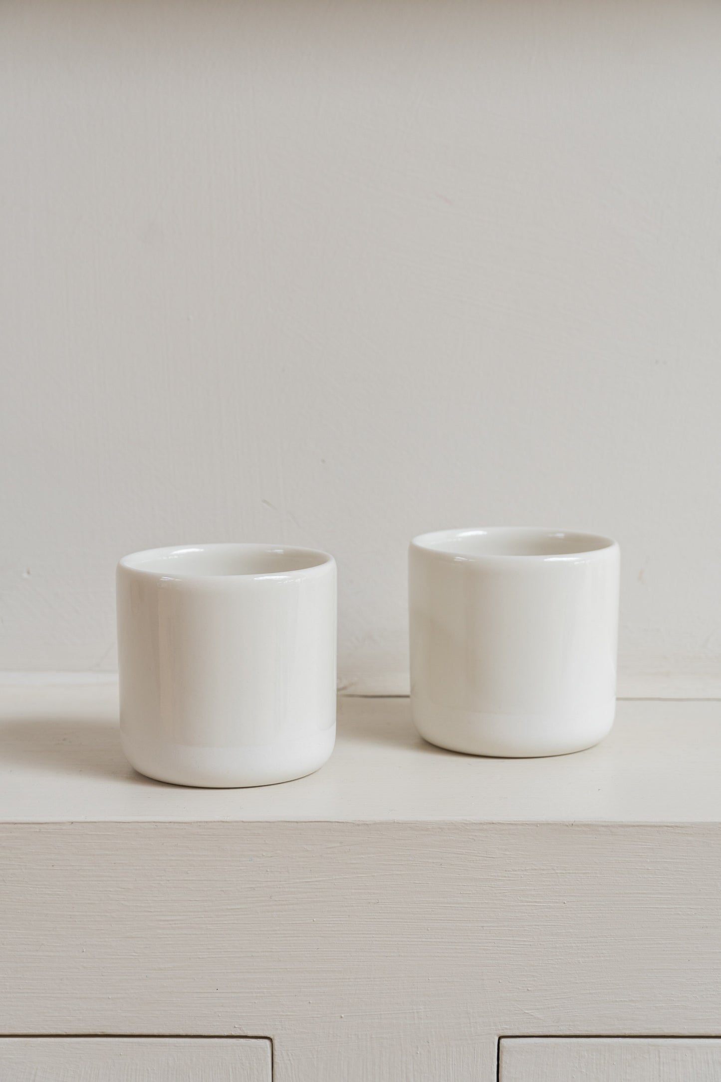 Two white Antibes Cups set on wall cabinet.
