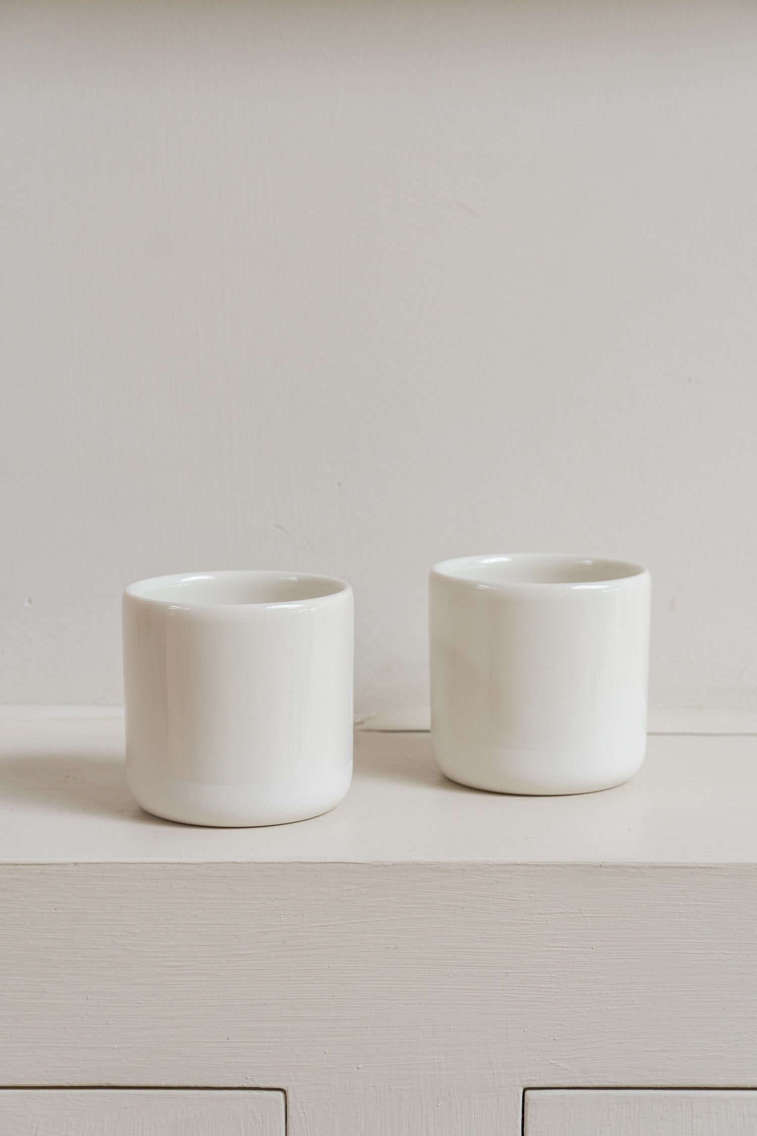 Two white Antibes Cups set on wall cabinet.
