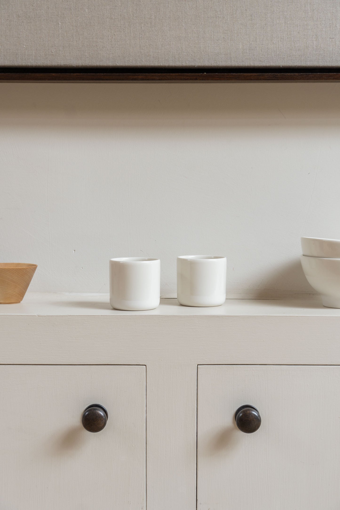 Two white Antibes Cups set on wall cabinet in white design interior.