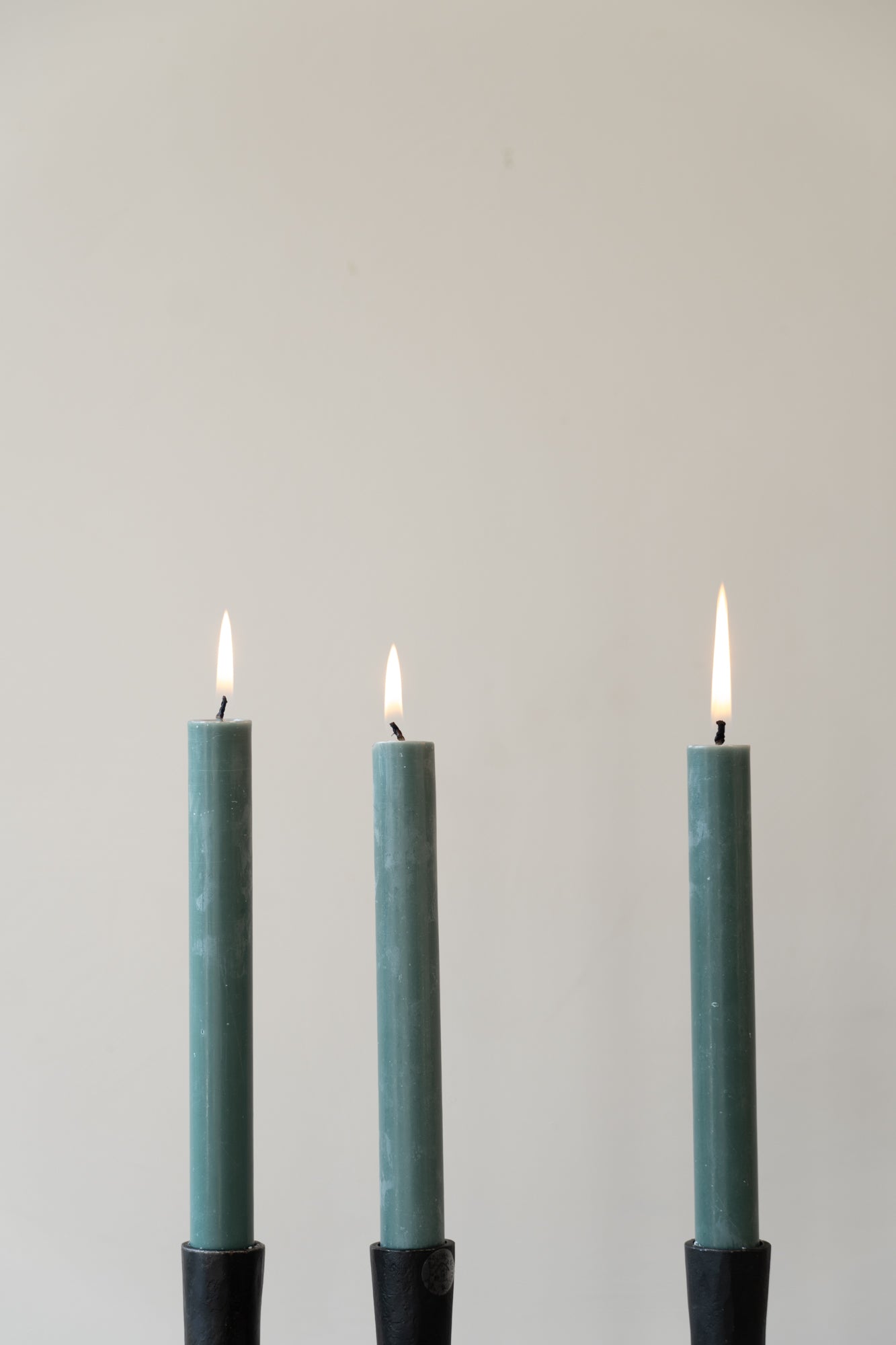 Three forest green lit dinner candles in black candle holders.