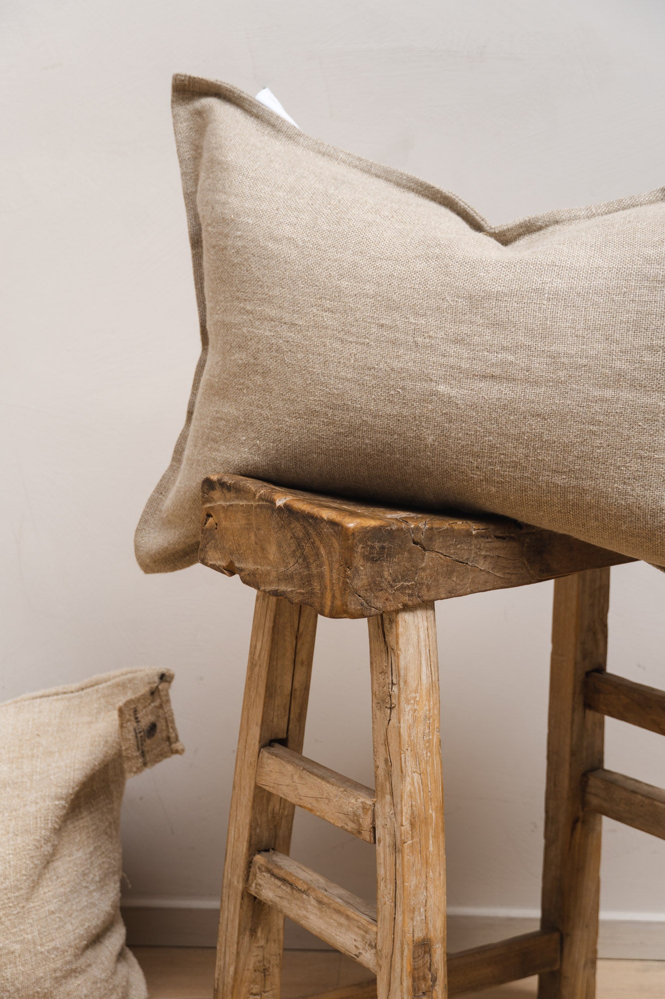 Details of the Linen Cushion Heavyweight Natural set on a wooden stool.