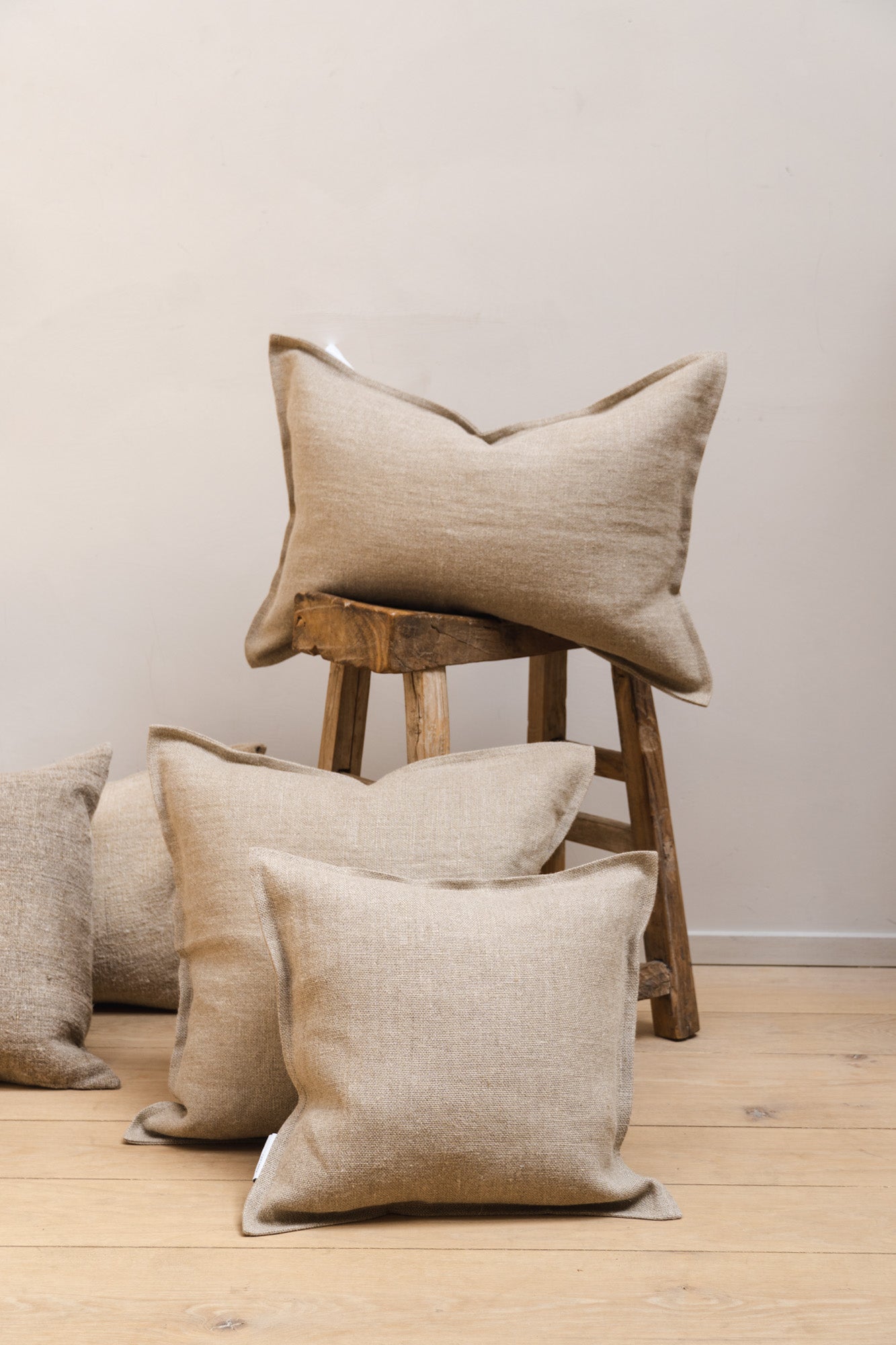 Beige-coloured natural linen cushions set on floor and wooden stool.
