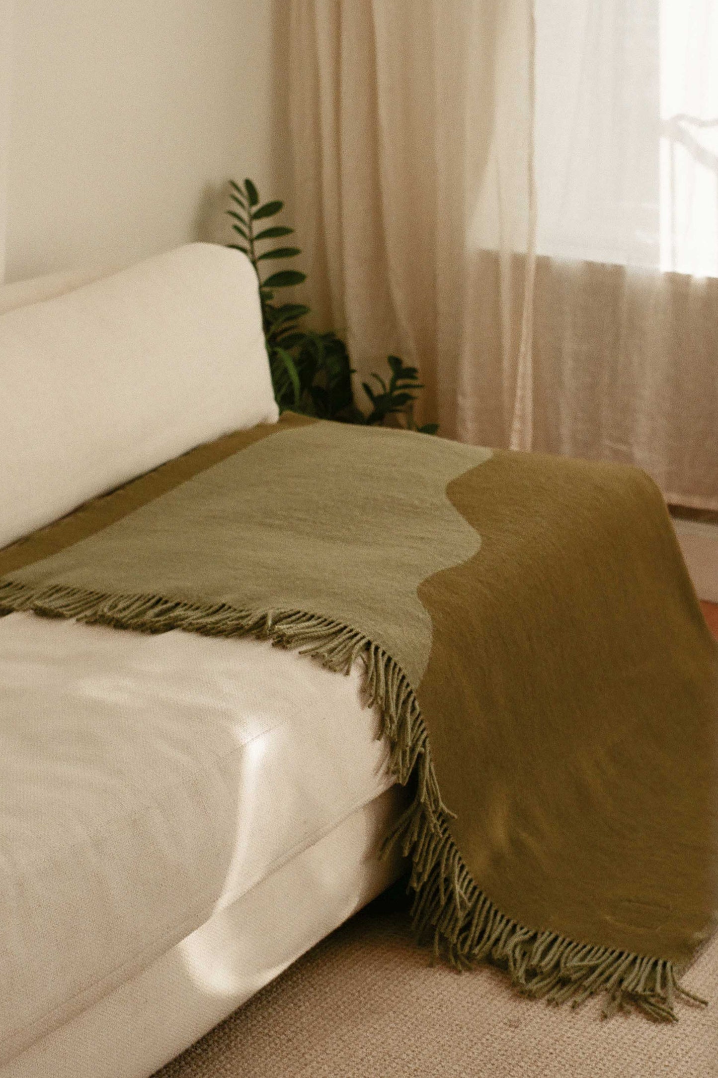 Moss Green Wool Blanket by Forestry Wool displayed on a sofa, adding a cosy and inviting touch to the neutral interior space.