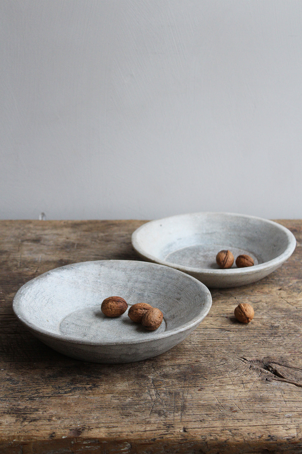 Two natural stone bowls on wooden table filled with walnuts.