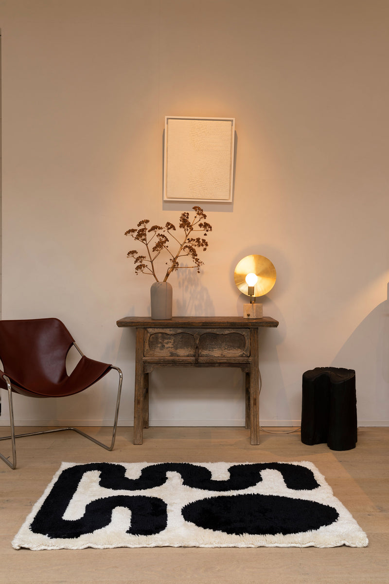 Saana Rug by Zakaria Rugs lying in front of a small wall table with decorations and Burned Chunk and Paulistano Chair at Enter The Loft.