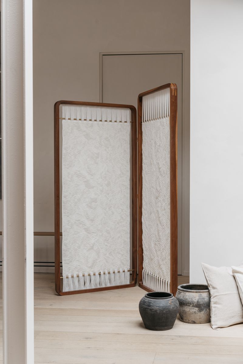 Aki Room Divider displayed, showcasing its ability to transform and define spaces. The intricate woven panels create a subtle pattern, complementing various interior styles.