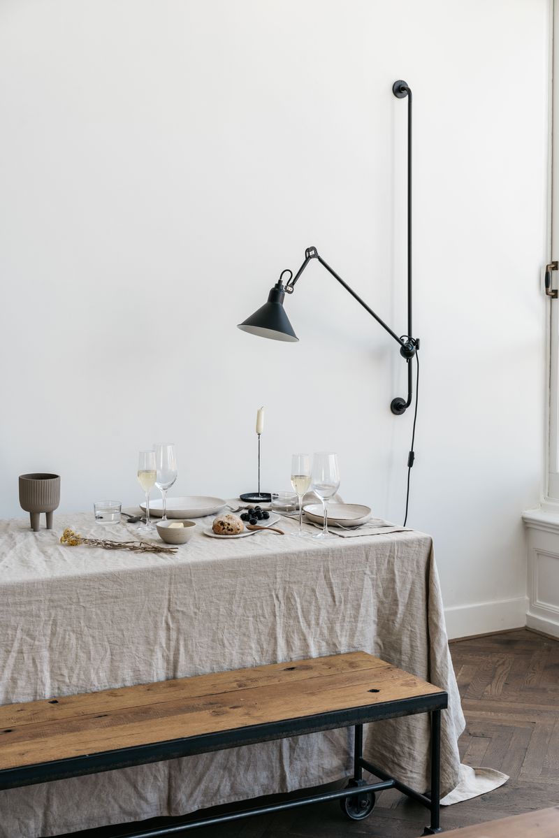 Lampe Gras N°214 by DCW Editions mounted on a white wall directed to illuminate a dinner table setting.