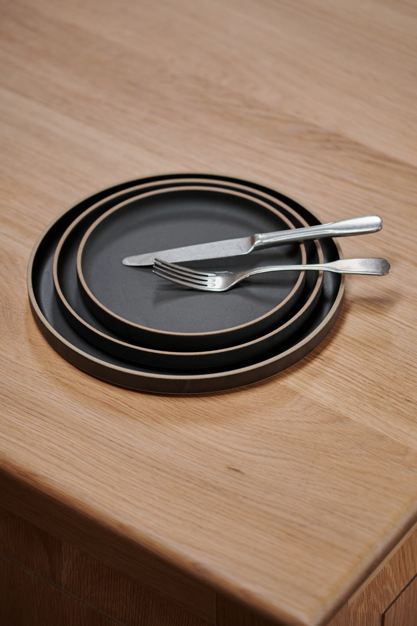 Black Ceramic Stackable Plates by Hasami Porcelain. Japanese style design, here seen with cutlery on a wooden table.