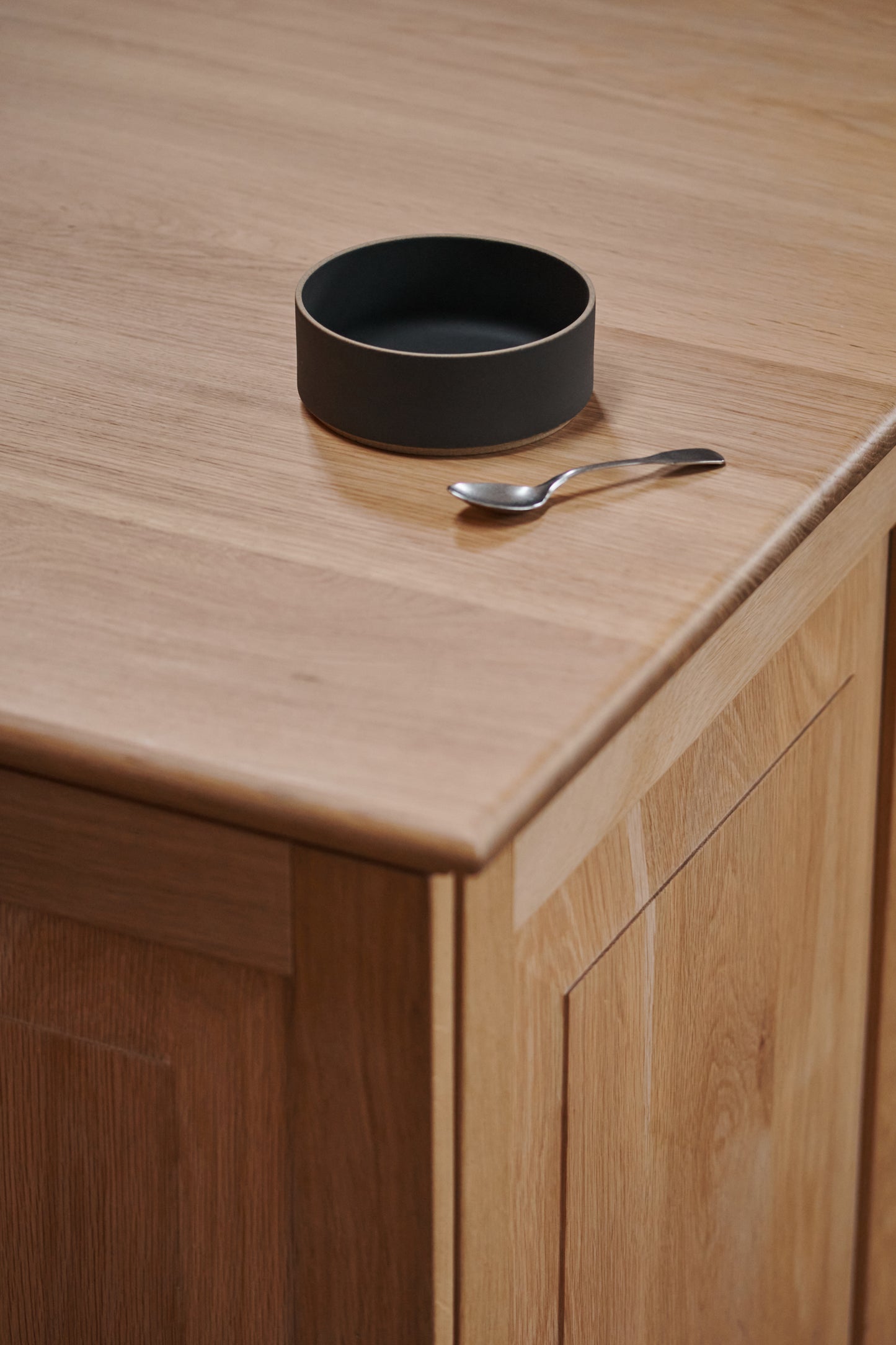 Black Ceramic Stackable Raised Bowl by Hasami Porcelain displayed on wooden tabletop kitchen interior with teaspoon next to it. Japanese-style design clay tableware.