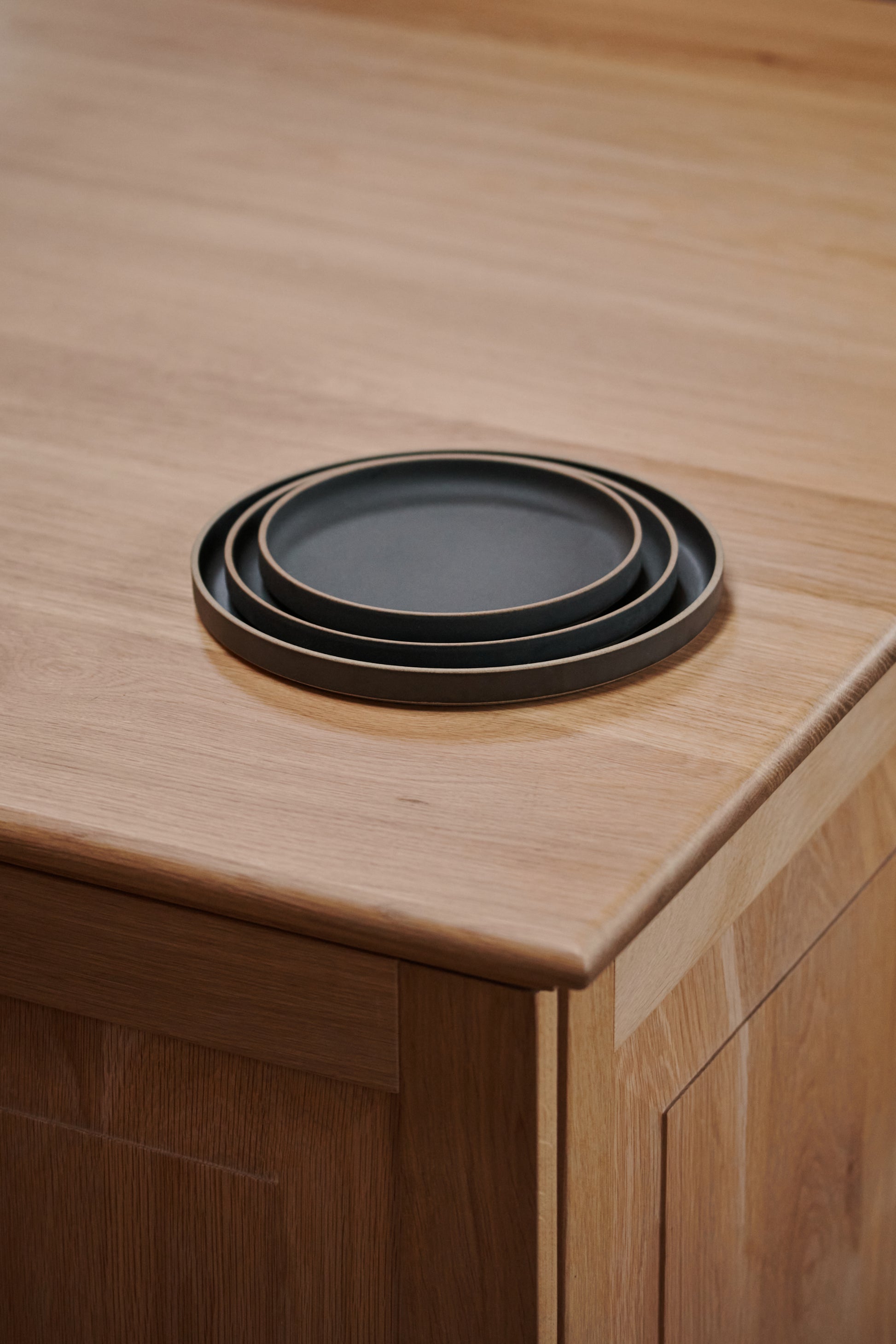 Black Ceramic Stackable Plates by Hasami Porcelain displayed on wooden tabletop kitchen interior. Japanese-style design clay tableware.