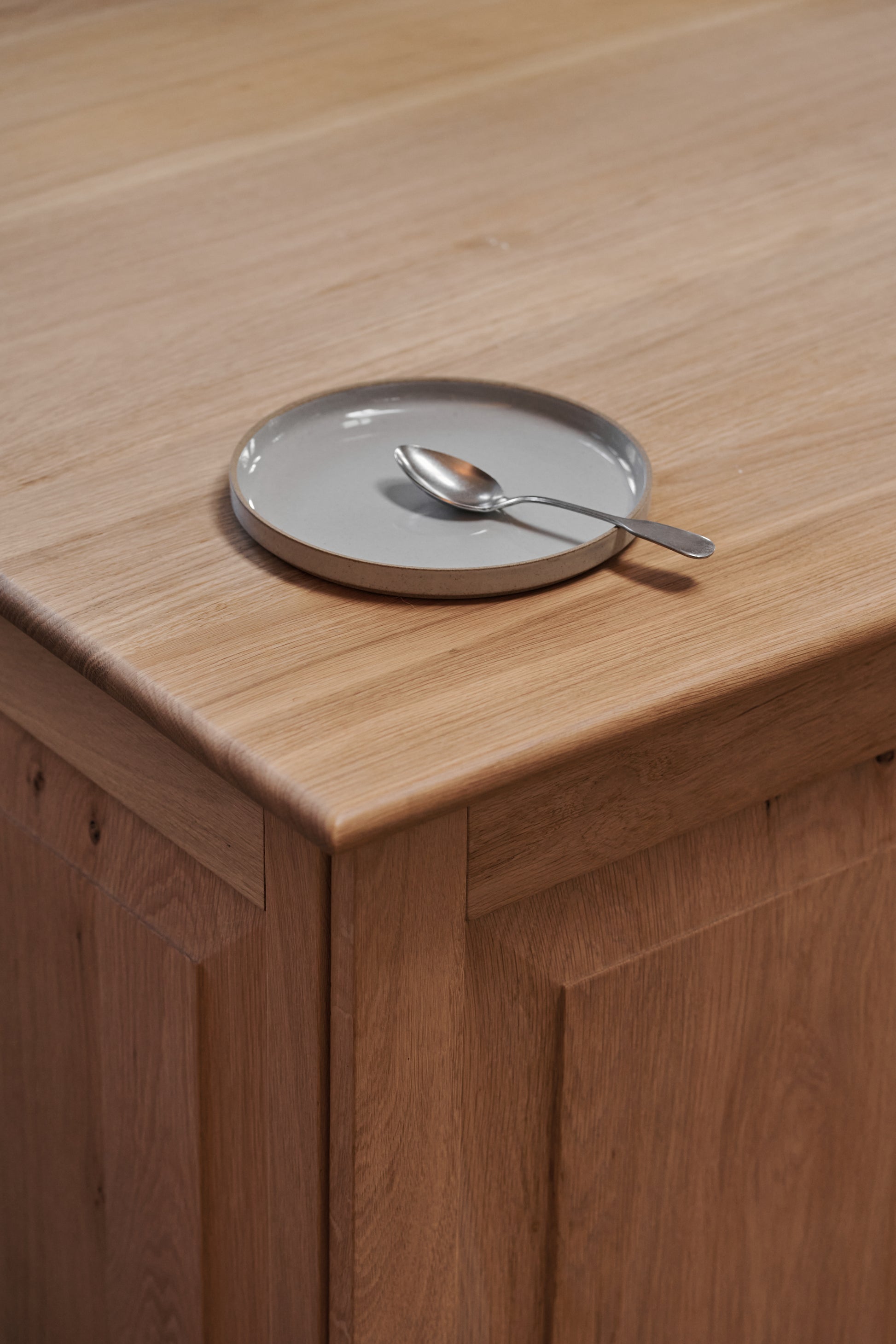 One grey ceramic stackable plate by Hasami Porcelain displayed on wooden tabletop kitchen interior with spoon on top. Japanese-style design clay tableware.