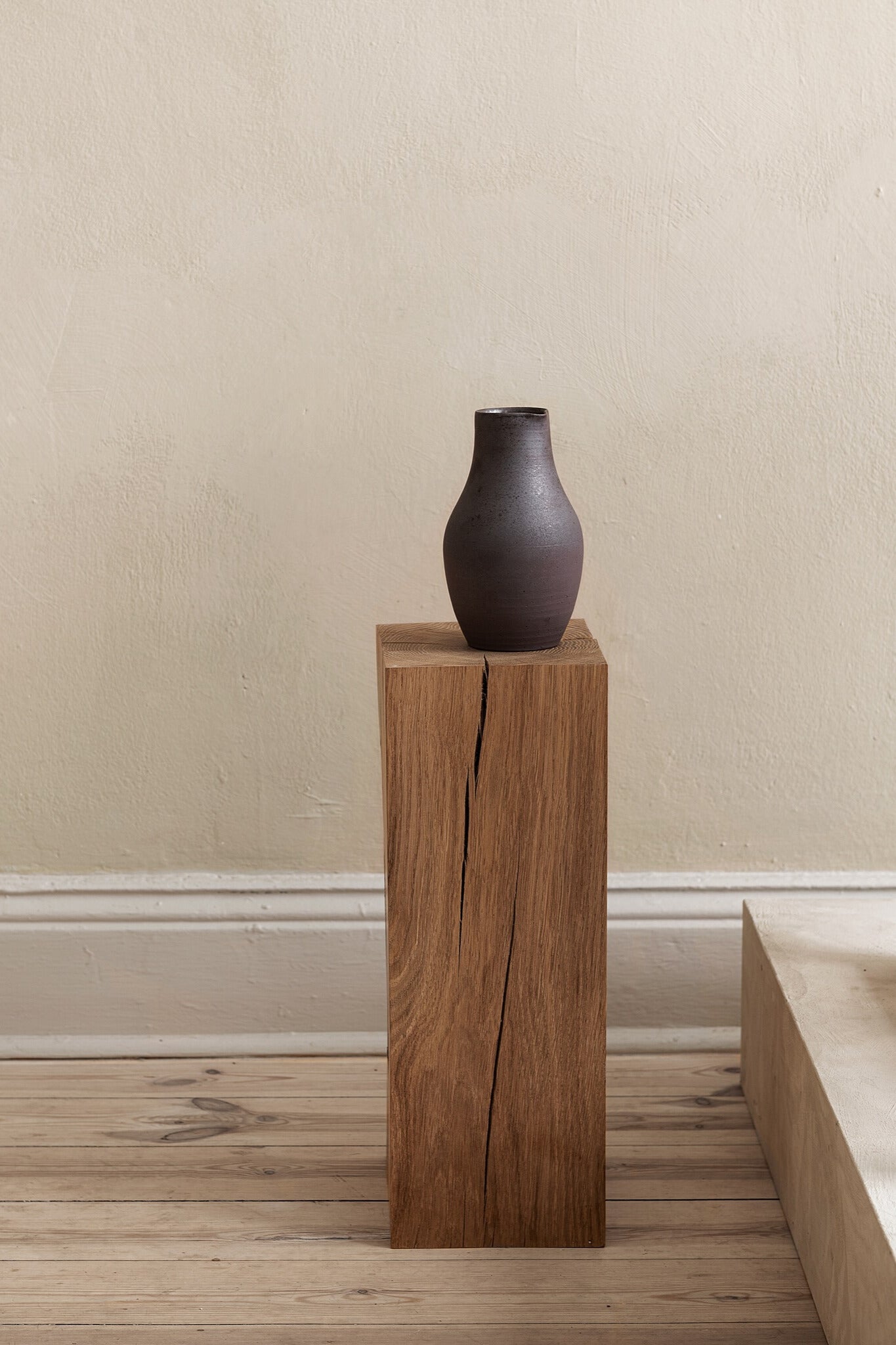 Black ceramic sake jug set on a display pedestal in neutral interior