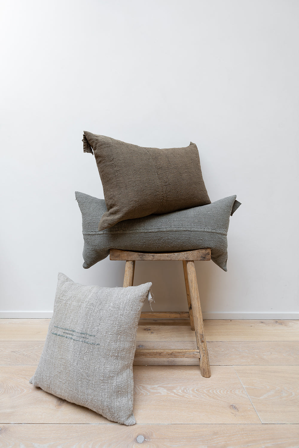Three linen cushions on wooden stool.